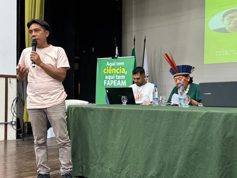Edinho Xamatari explicando a dissertação e Paulo Roberto Sousa e Davi Kopenawa ao fundo
