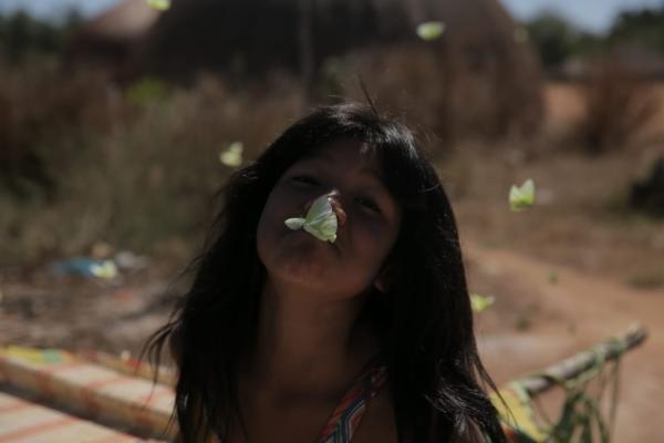 Jepi Kaiulu Kalapalo brinca alegremente com borboletas em frente à sua casa na Aldeia Kalapalo, Terra Indígena do Xingu|Tauana Kalapalo/2016